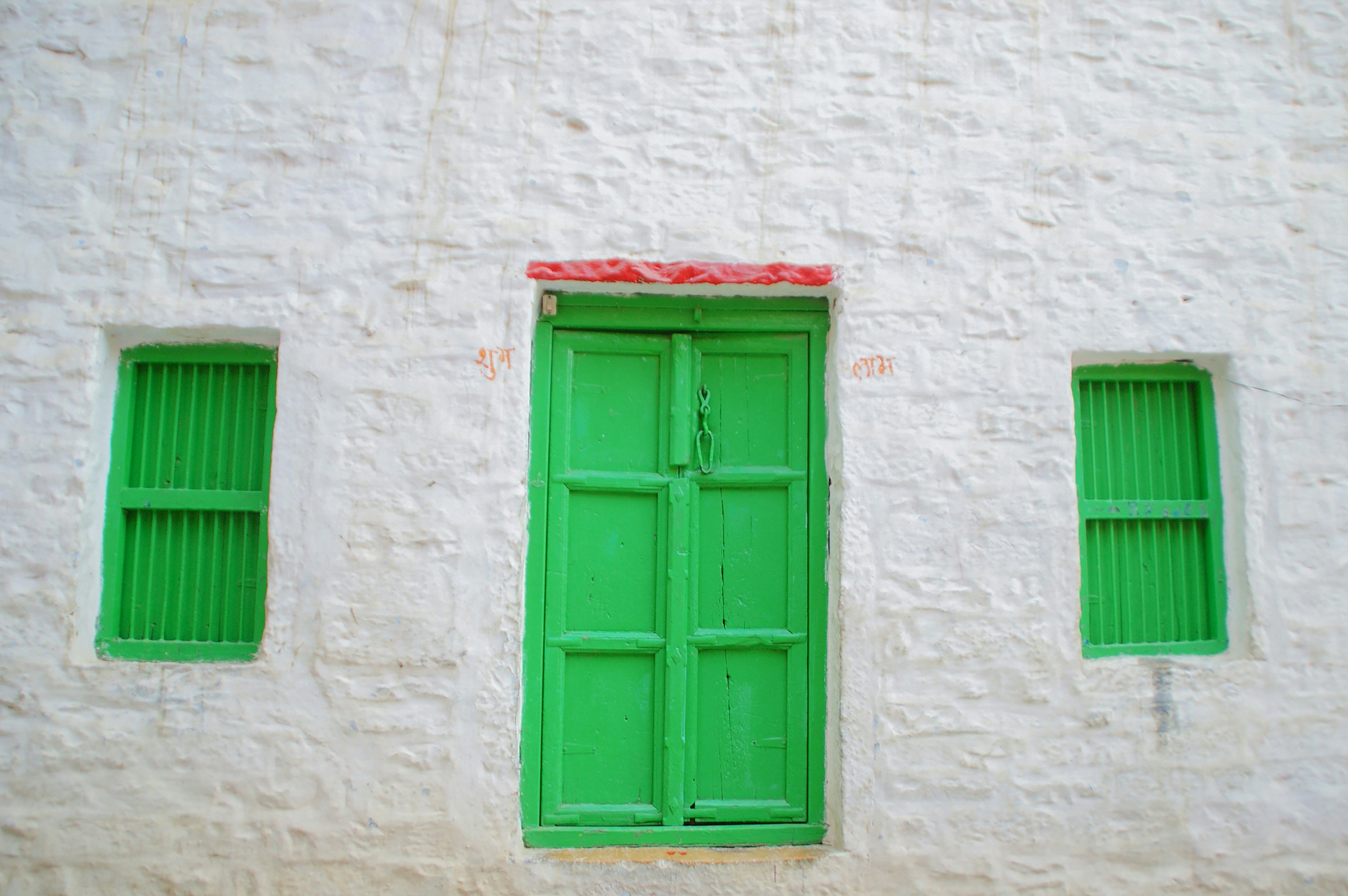 A whitewashed wall with a painted green door and shuttered windows